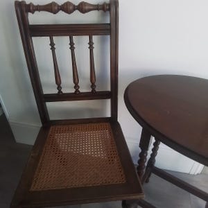 Puede incluir: Una silla de madera marr&oacute;n oscuro con un asiento de ca&ntilde;a tejido y una mesa de madera marr&oacute;n oscuro a juego con una tapa redonda.