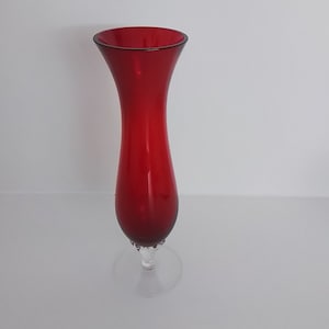 May include: A tall, slender red glass vase with a clear glass base. The vase has a rounded top and a slightly flared bottom.