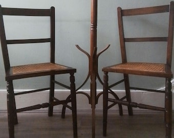 May include: Two wooden chairs with cane seats and a wooden coat rack stand in front of a light green wall.