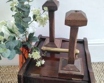 May include: A wooden boot jack with two wooden boot lifts. The boot jack is dark brown and has a brass handle. The boot lifts are also dark brown and have a square base.