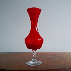 May include: A red glass vase with a clear glass base. The base has a twisted design.