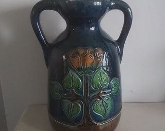 May include: A blue ceramic vase with two handles and a floral design. The vase features a stylized flower with orange and yellow petals and green leaves.