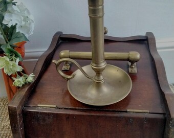 May include: A brass candlestick with a decorative handle and a round base sits on top of a wooden box with a hinged lid. The candlestick is made of polished brass and has a simple design.