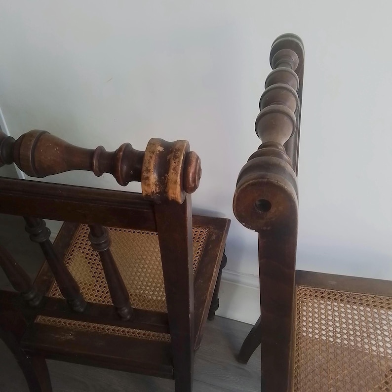Puede incluir: Dos sillas de madera con asientos de ca&ntilde;a. Las sillas tienen  tornillos torneados y un acabado marr&oacute;n oscuro.