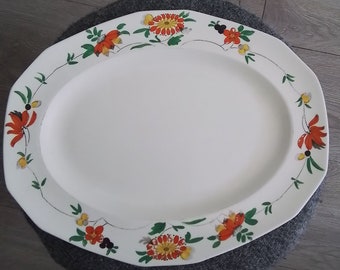 May include: White oval serving platter with a decorative floral border. The border features orange, yellow, and green flowers with black accents.