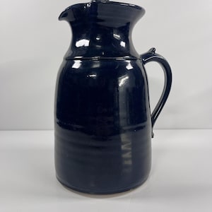 May include: A dark blue ceramic pitcher with a wide mouth and a handle. The pitcher has a smooth, glossy finish.