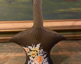 May include: A brown glass vase with a twisted handle and a floral design painted on the front. The vase is decorated with yellow, orange, white, and blue flowers.