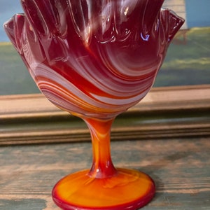May include: A red, white and orange swirl glass candy dish with a ruffled rim and a pedestal base.