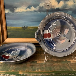 May include: Two blue ceramic serving dishes with white and red painted designs. The larger dish has two handles and is on a clear stand. The smaller dish is a bowl.