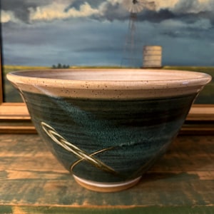 Puede incluir: Un tazón grande, profundo, de cerámica con un esmalte verde y un borde blanco. El tazón tiene un diseño sutil de finas líneas doradas en la superficie.