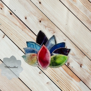 May include: A set of seven reusable makeup remover pads in various colors, including blue, green, red, and purple. The pads are arranged in a flower shape on a wooden surface. The text "TKR Reusables!" is visible in the lower left corner of the image.