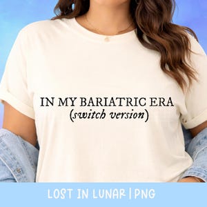 May include: Cream-colored t-shirt with the text "IN MY BARIATRIC ERA (switch version)" in black. The shirt has rolled-up sleeves and is paired with a denim jacket. The bottom of the image has the text "LOST IN LUNAR | PNG".
