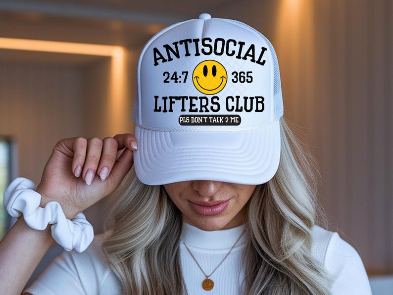 Puede incluir: Gorra de camionero blanca con el texto "ANTISOCIAL 24:7 365 LIFTERS CLUB PLS DON'T TALK 2 ME" en negro, una carita sonriente amarilla y una parte trasera de malla blanca.