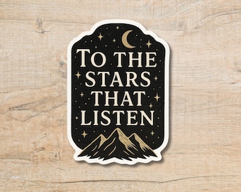 May include: A sticker with a black background and white text that reads "TO THE STARS THAT LISTEN." The sticker features a crescent moon, stars, and mountain silhouettes. The sticker has a white border and is on a wooden surface.