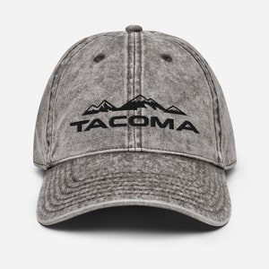 May include: A gray distressed denim baseball cap with a black embroidered mountain range and the word "TACOMA" underneath.