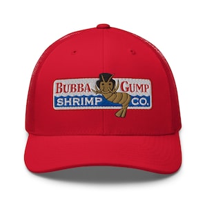 May include: A red trucker hat featuring the Bubba Gump Shrimp Co. logo. The logo is an embroidered patch with the company name and a cartoon shrimp wearing a hat. The hat has a mesh back and a curved brim.