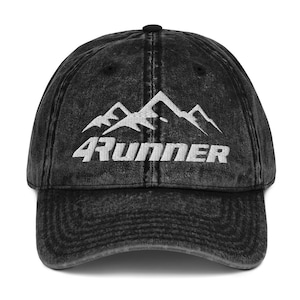 Puede incluir: Gorra de béisbol negra de estilo vintage con visera curva. La gorra presenta un gráfico de montaña blanco sobre la palabra "4RUNNER" en negrita, fuente sans-serif. La gorra tiene un aspecto desgastado.