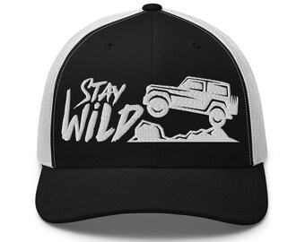 May include: Black and white trucker hat with a mesh back. The front panel features the words "Stay Wild" in white script, along with a white graphic of a 4x4 vehicle. The hat has a curved brim and a snapback closure.