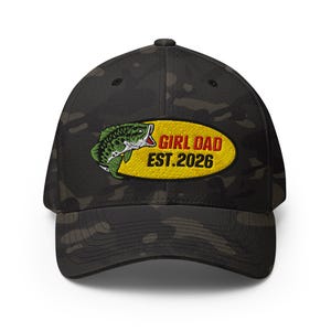 May include: A black camouflage baseball cap featuring an embroidered oval patch on the front. The patch displays a green fish graphic next to the red and black text "GIRL DAD EST.2026" set against a yellow background on the cap's front panel.