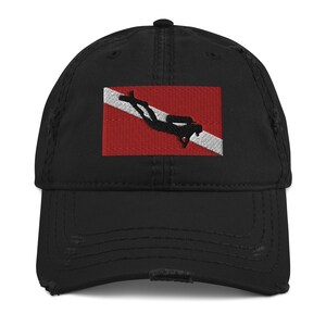 May include: Black distressed baseball cap featuring an embroidered scuba diving flag. The flag design includes a red background, a white diagonal stripe, and a black diver silhouette. The cap has a pre-curved visor.