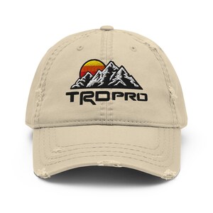 May include: A beige baseball cap with a worn brim. The cap displays an embroidered design of mountains, a setting sun, and the word "TROPRO" in black, block letters.