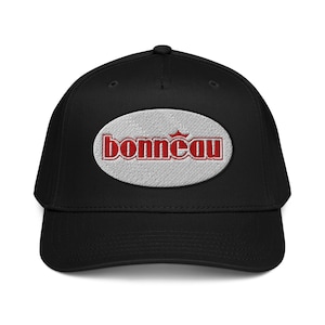 Könnte beinhalten: Schwarze Baseballkappe mit gebogenem Schirm. Die Kappe hat einen gestickten ovalen Aufnäher mit dem Wort "bonnéau" in roter Schrift. Der Aufnäher ist vor einem strukturierten, hellgrauen Hintergrund angebracht.