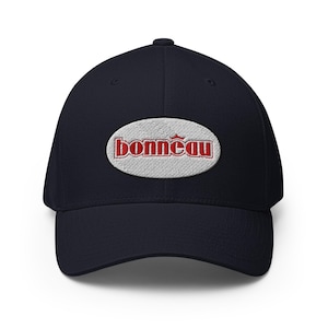 Könnte beinhalten: Marineblaue Baseballkappe mit gebogenem Schirm. Auf der Kappe befindet sich ein gesticktes ovales Patch mit dem Wort "Bonneau" in roter Schrift. Der Patch ist rot umrandet und hat ein Kronensymbol über dem "o".