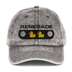 May include: A gray, distressed baseball cap with the word "RENEGADE" embroidered in black above a black rectangle. Inside the rectangle are two yellow rubber duckies. The cap has a curved brim and a button on top.
