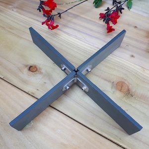 May include: A grey metal plant stand with four legs that form an X shape. The stand is made of metal and has a grey finish. The stand is on a wooden surface.