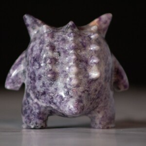 Pu&ograve; includere: Una piccola figurina in ceramica, di colore viola e bianco, con punte, corpo arrotondato e superficie testurizzata.