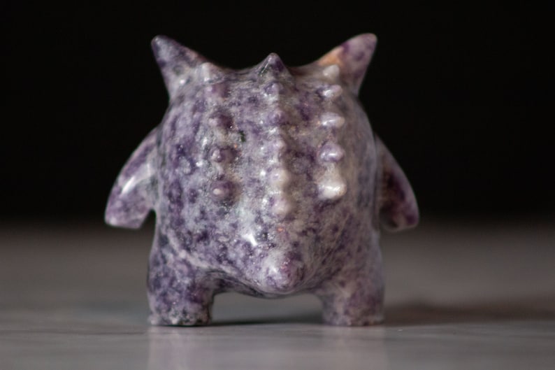 Pu&ograve; includere: Una piccola figurina in ceramica, di colore viola e bianco, con punte, corpo arrotondato e superficie testurizzata.