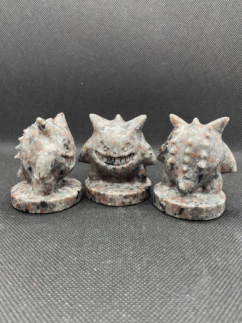 Pu&ograve; includere: Tre piccole figurine di pietra scolpite a mano di un personaggio Pokemon. Le figurine sono grigie con macchie nere e hanno un'espressione minacciosa.