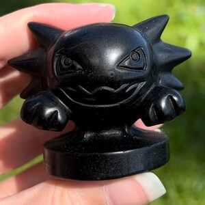 Pu&ograve; includere: Una piccola statuina dettagliata di un personaggio Pokemon scolpita in ossidiana nera. La statuina ha un'espressione minacciosa con denti aguzzi e occhi grandi.