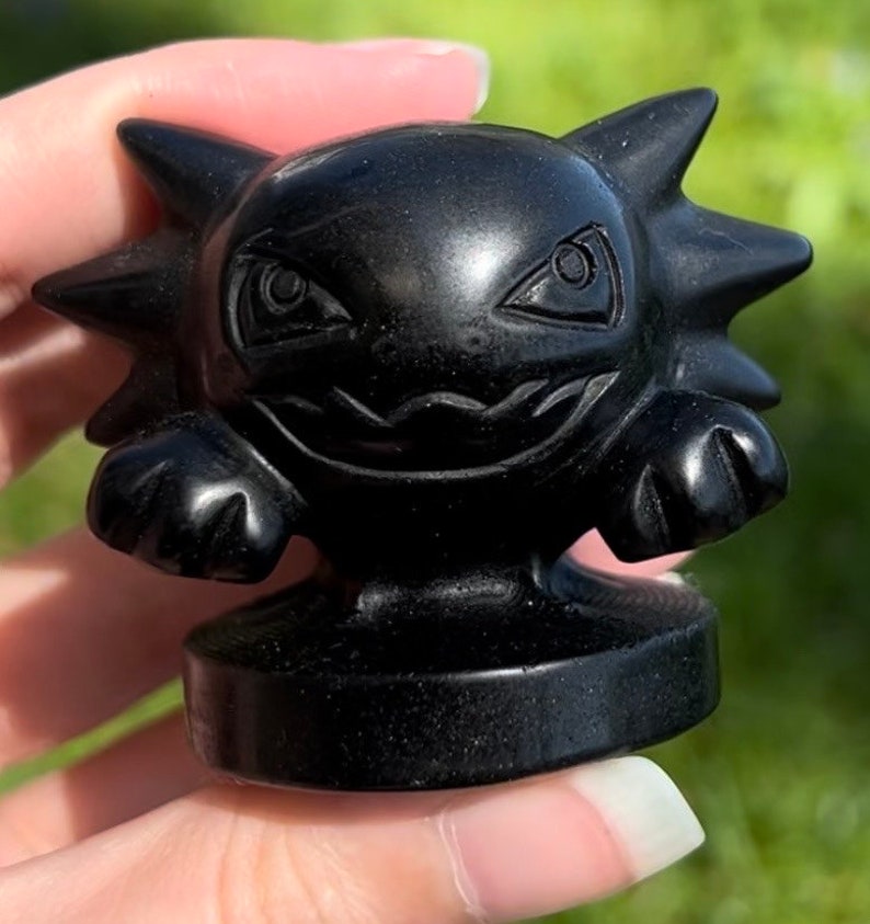 Pu&ograve; includere: Una piccola statuina dettagliata di un personaggio Pokemon scolpita in ossidiana nera. La statuina ha un'espressione minacciosa con denti aguzzi e occhi grandi.