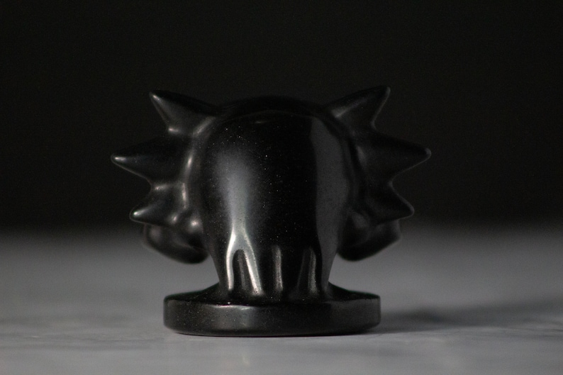 Pu&ograve; includere: Una scultura in ceramica nera di un drago con la schiena e la testa spinose. Il drago &egrave; rivolto in avanti con la bocca chiusa.
