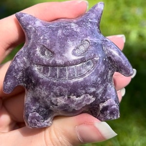 Pu&ograve; includere: Una statuetta di cristallo intagliata di colore viola e bianco che rappresenta un fantasma dei cartoni animati con un ampio sorriso e grandi occhi.