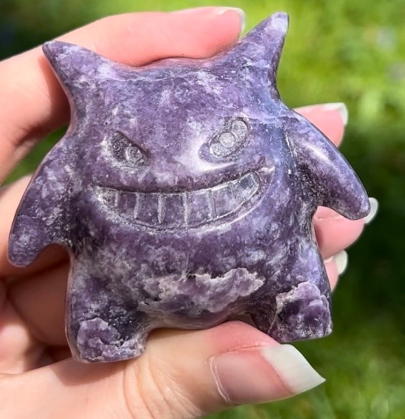 Pu&ograve; includere: Una statuetta di cristallo intagliata di colore viola e bianco che rappresenta un fantasma dei cartoni animati con un ampio sorriso e grandi occhi.