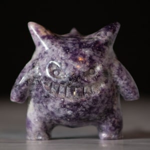 Pu&ograve; includere: Figurina di cristallo viola e bianco di un mostro dei cartoni animati con un ampio sorriso. La figurina &egrave; alta circa 7,5 cm e ha una superficie dettagliata e testurizzata.
