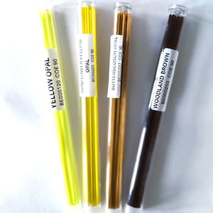 May include: Four glass tubes containing colorful glass rods. The tubes are labeled with the colors: Yellow Opal, Sunflower Yellow Opal, Butterscotch Opal, and Woodland Brown. The labels also include the codes BE000120, BE000220, BE000337, and BE000203.