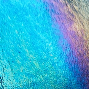 May include: Abstract image with a textured surface, featuring a gradient of colors. The dominant hues are shades of blue, transitioning into areas of purple, pink, and yellow. The surface has a subtle, rippled appearance.