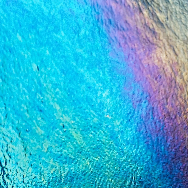May include: Abstract image with a textured surface, featuring a gradient of colors. The dominant hues are shades of blue, transitioning into areas of purple, pink, and yellow. The surface has a subtle, rippled appearance.