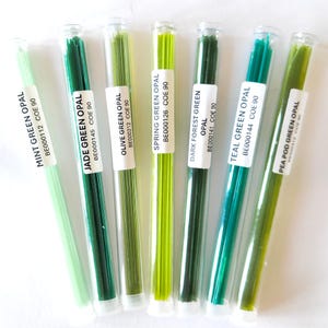 May include: Seven glass tubes filled with green glass rods. Each tube has a white label with the name of the color and the text "COE 90". Colors include Mint Green, Jade Green, Olive Green, Spring Green, Dark Forest Green, Teal Green, and Pea Pod Green.