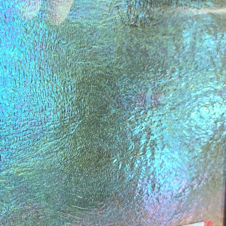 May include: Abstract close-up of a textured surface with iridescent qualities. The surface displays a blend of blue, green, and purple hues, creating a shimmering effect. The texture appears to have a rippled or wave-like pattern.