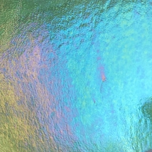 May include: Abstract close-up of a shimmering, iridescent surface. The colors shift from green to blue and purple, creating a textured, oil slick effect. The surface appears to be slightly rippled, adding depth.