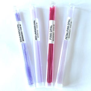 May include: Four glass tubes containing colorful glass rods. The tubes are labeled with the names of the colors: Gold Purple Opal, Neo-Lavender Opal, Pink Opal, and Petal Pink Opal. The rods are various shades of purple and pink.