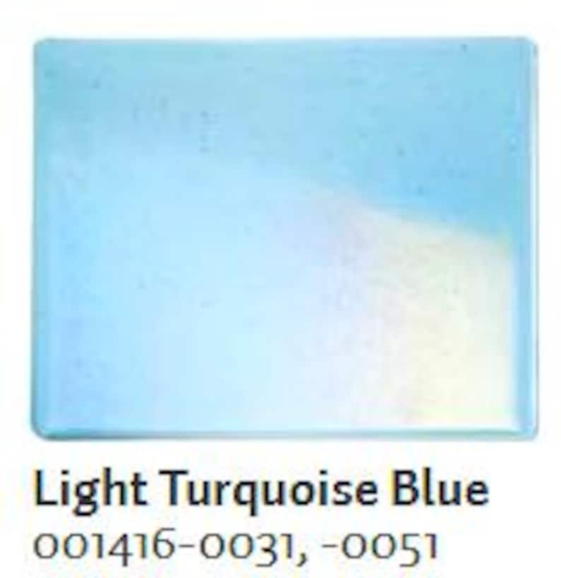 May include: A square, light turquoise blue glass tile. The tile has a glossy finish and rounded edges. The text "Light Turquoise Blue" is printed below the tile, along with the numbers 001416-0031, -0051.