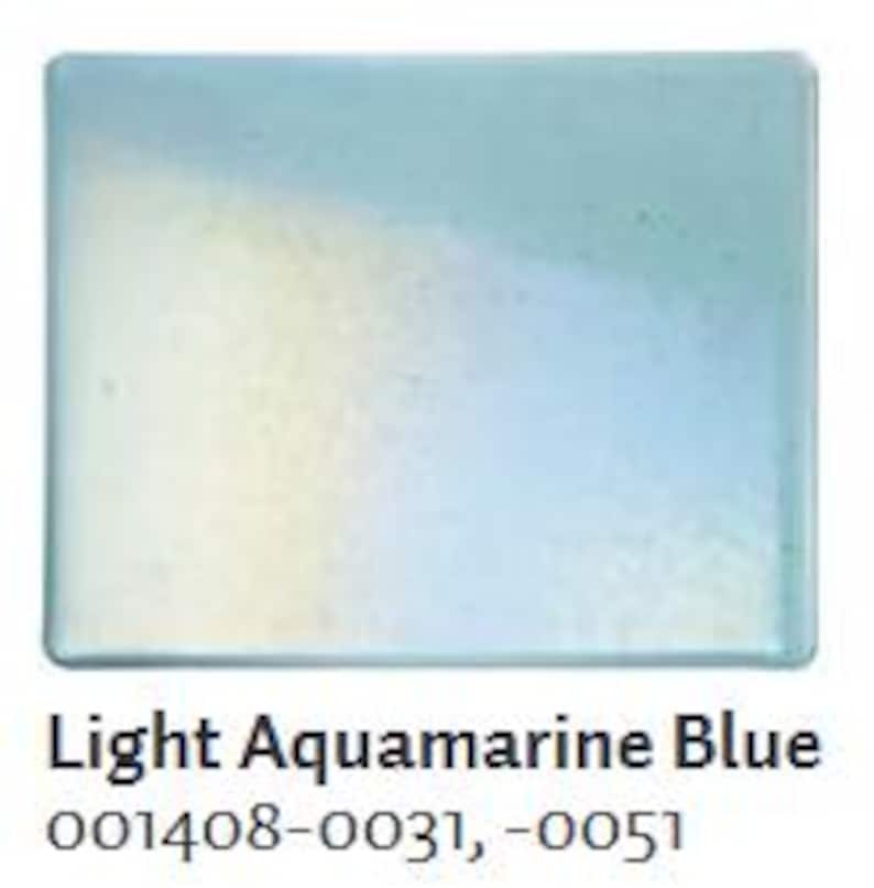 May include: A rectangular, light aquamarine blue glass tile. The tile has a glossy finish and a subtle gradient of color. The text "Light Aquamarine Blue" is printed at the bottom, along with the product codes.
