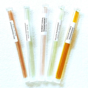 May include: Five glass tubes containing transparent glass rods in various colors: red, orange, sunset coral, yellow, and medium amber. Each tube has a white label with the color name and product code.