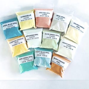 May include: An assortment of small, clear plastic bags filled with colorful opal powders. Each bag is labeled with the opal's name and powder details. Colors include blue, yellow, orange, green, and pink. The bags are arranged on a white surface.