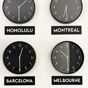 May include: Four black analogue clocks with white hands and numbers, showing different times. The clocks are labelled with the cities Honolulu, Montreal, Barcelona, and Melbourne.